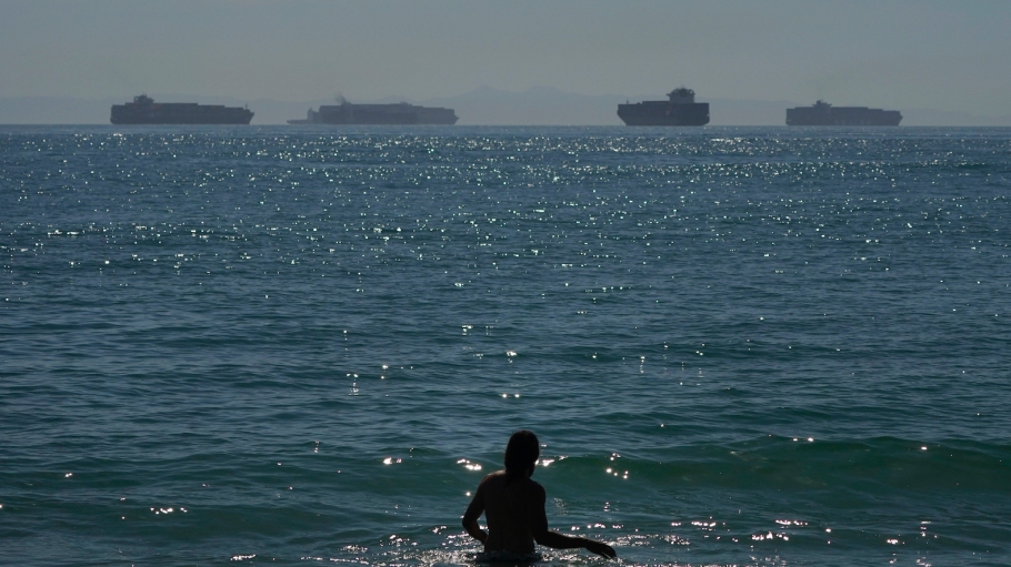 beplay官网娱乐男人涉水通过水密封加州海滩码头集装箱船等待在洛杉矶港口和长滩的距离。