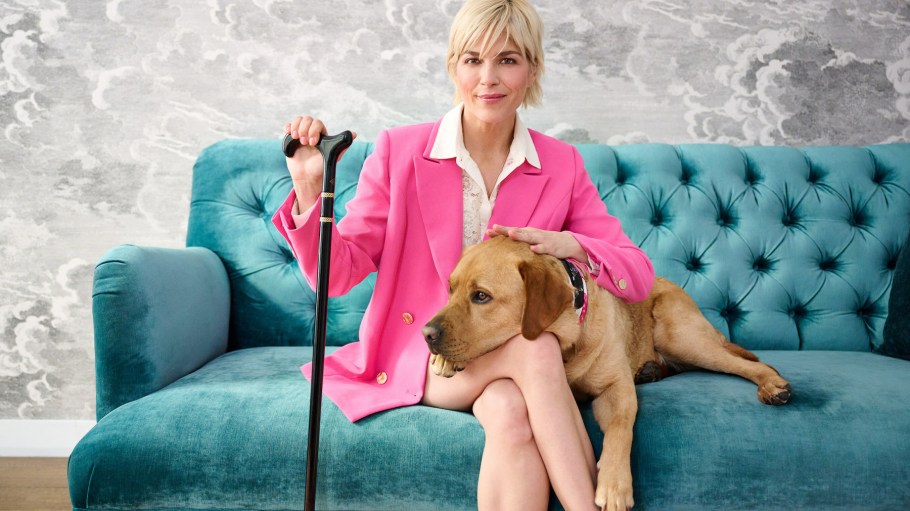 beplay官网娱乐塞尔玛布莱尔,QVC品牌大使的可访问性,坐在豪华的蓝绿色沙发与她的狗,童子军beplay手机官网下载。beplay官网娱乐她穿着一件粉红色西装,使用黑色和金色的手杖。